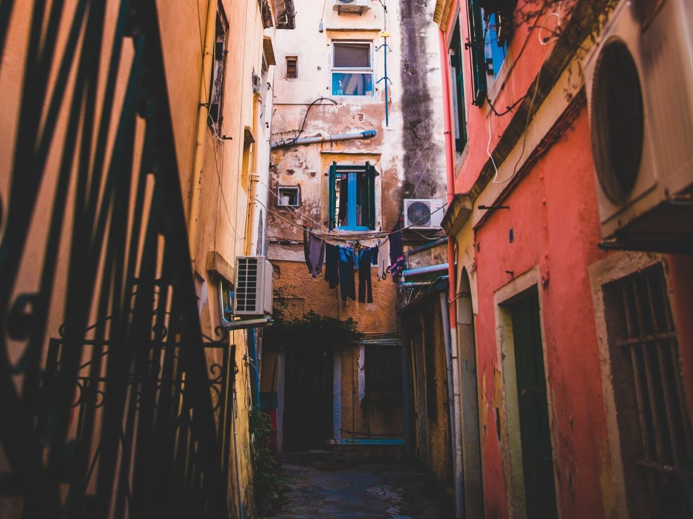 Callejón en Portugal con unidades de aire acondicionado, mostrando eficiencia energética y reducción de costos inmobiliarios. Arquitectura antigua y ropa tendida.