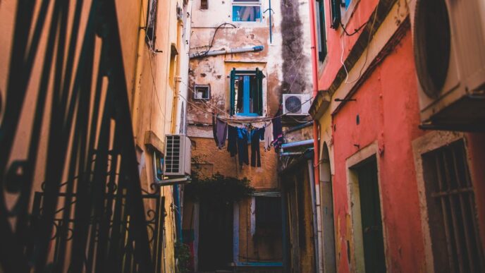 Callejón en Portugal con unidades de aire acondicionado, mostrando eficiencia energética y reducción de costos inmobiliarios. Arquitectura antigua y ropa tendida.