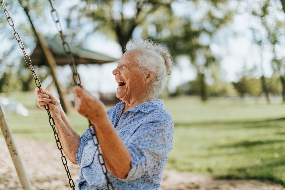 Una mujer mayor ríe mientras se balancea en un columpio. El real estate ofrece espacios para todas las edades. Inmobiliare Summits.