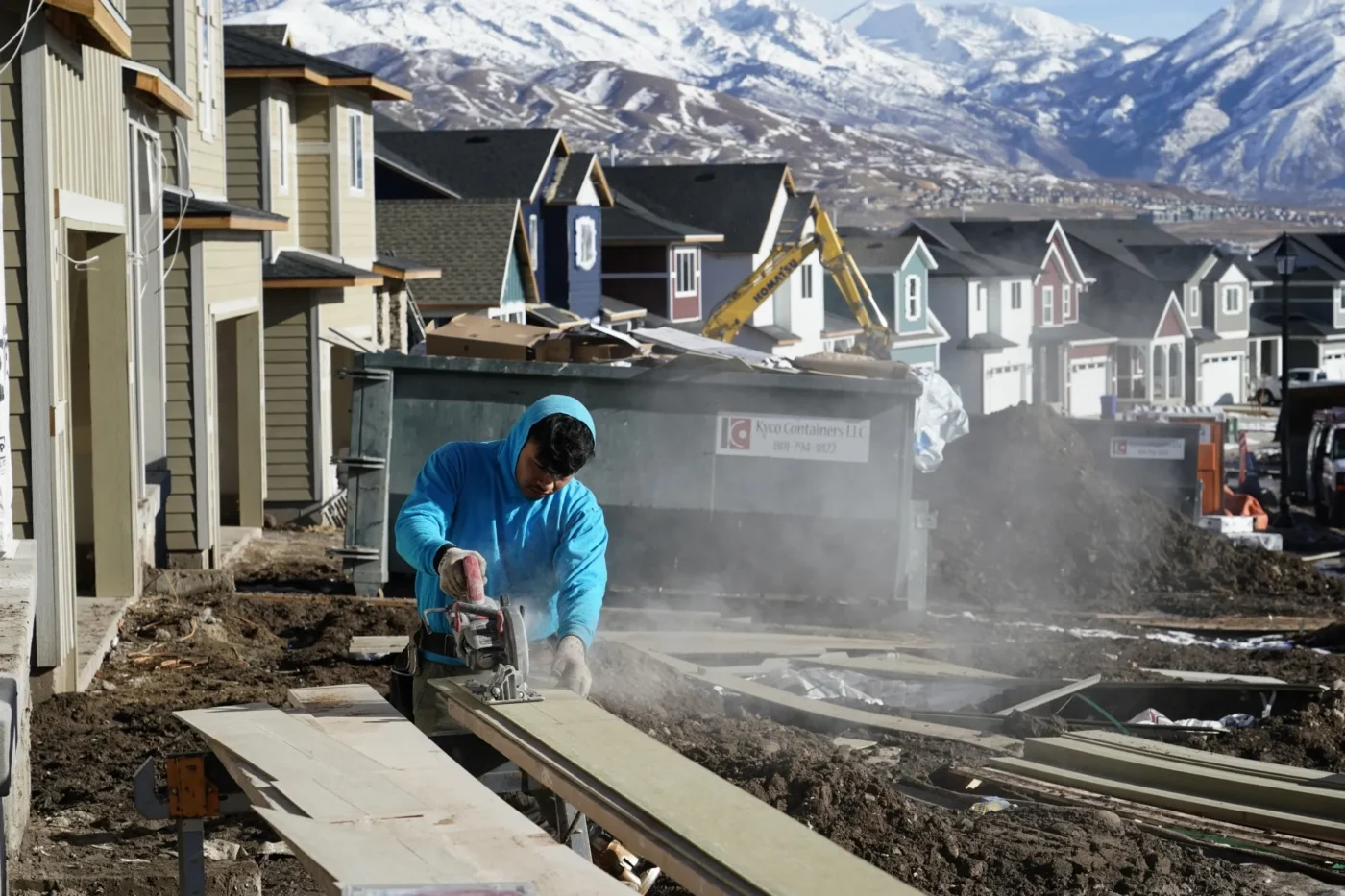 Trabajador corta madera en obra de construcción de viviendas en Estados Unidos, con montañas nevadas al fondo. Aumento del 6.8% en febrero.