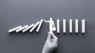 Conceptual: Deteniendo el efecto dominó. Mano sosteniendo figura de persona que impide la caída de bloques. Implicaciones en real estate, México.