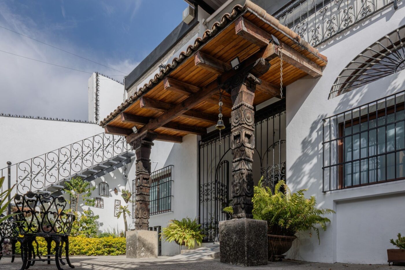 Fachada de casa en Guadalajara con pilares de madera tallada, vegetación y cielo azul. Interés creciente en adquirir propiedades en Guadalajara.