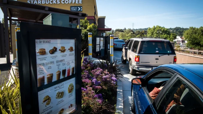 Tendencia Drive Thru: Cola de autos en Starbucks, menú digital visible con opciones de desayuno, café y postres. Comida rápida en la frontera.