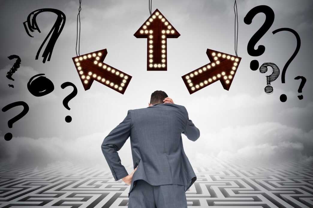 Concepto inmobiliario: Hombre confundido ante flechas y signos de interrogación sobre un laberinto. Incertidumbre económica en LATAM.