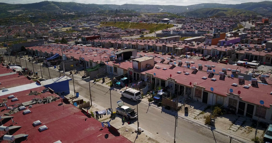 Vista aérea de viviendas en México, mostrando desafíos inmobiliarios: costos y proyectos. Casas rojas, paisaje urbano denso y colinas al fondo.