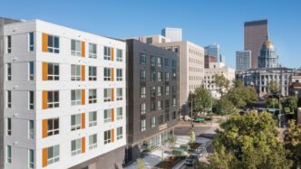 Edificio moderno en Denver, diseño de vivienda asequible con toques naranjas y vistas al capitolio. Arquitectura sostenible e innovadora en primer plano.