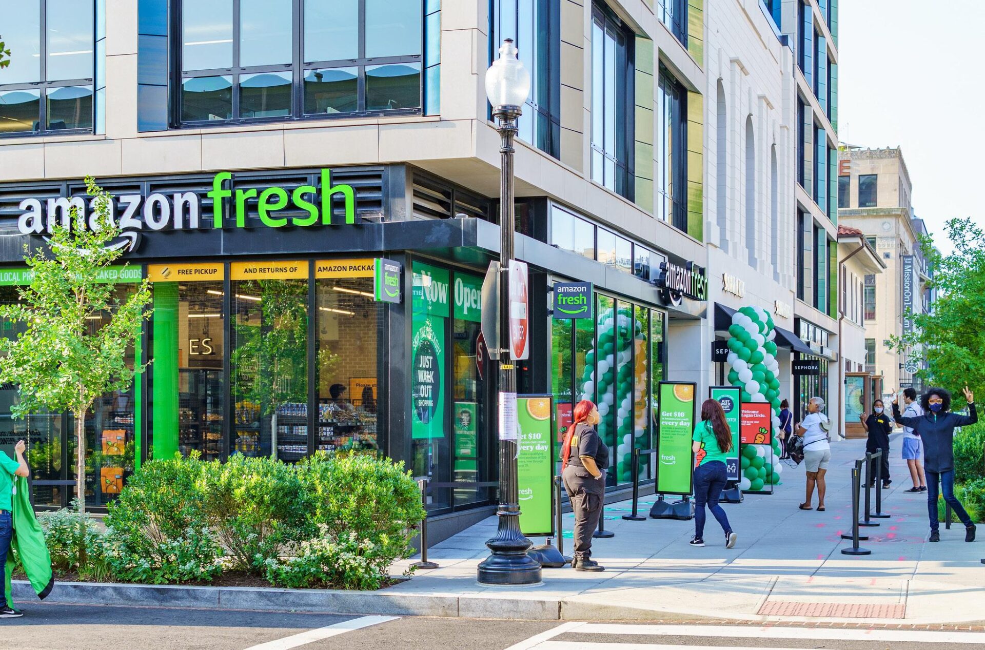 Tienda Amazon Fresh en Glendale con gente esperando. Estrategias de mercado en desinversión y oportunidades visibles. Fachada moderna y letreros verdes.