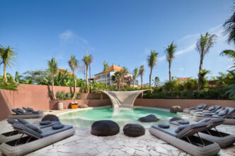 Piscina de hotel sostenible en Bali con tumbonas, rocas y palmeras. Un oasis de relajación comprometido con la sostenibilidad hotelera en Bali.