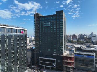 Vista del Edificio Sinergia Faro, con certificación LEED Platino, destacando su diseño moderno y sostenible. Arquitectura urbana, cielos azules.
