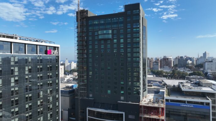 Vista del Edificio Sinergia Faro, con certificación LEED Platino, destacando su diseño moderno y sostenible. Arquitectura urbana, cielos azules.