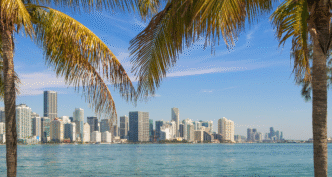 City/Destination
Miami, destino de Inmobiliare Summits. Vista del horizonte urbano y el mar, palmeras en primer plano. El auge inmobiliario atrae inversores LATAM.