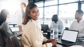 Mujer emprendedora en reunión de real estate, sonriendo. Laptop, equipo diverso. El poder transformador en bienes raíces en acción, inspirador.