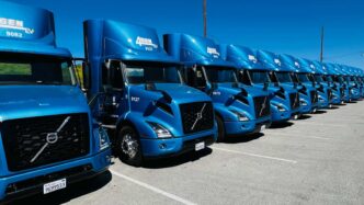 Fila de camiones eléctricos azules, parte de la electromovilidad para una logística cero contaminante. Volvo y Agen EV destacan en la flota.