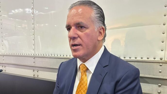 Hombre con traje hablando sobre la inversión de la empresa automotriz en Toluca, promoviendo la expansión y el desarrollo económico local.