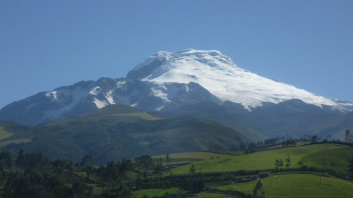 Vista panorámica del nevado Chimborazo, con su cumbre cubierta de nieve brillante, resaltando sobre las colinas verdes y el cielo azul despejado.
