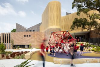 Vista de la Escuela Darlington en Australia, nombrada mejor edificio 2024. Niños jugando en la estructura roja. Arquitectura moderna y espacio lúdico.