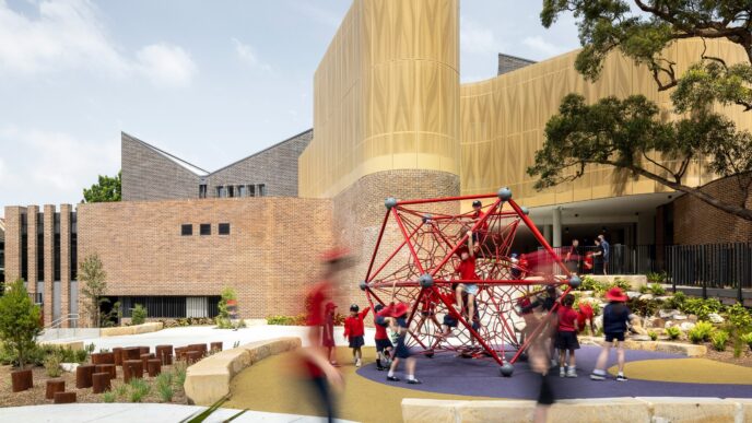 Vista de la Escuela Darlington en Australia, nombrada mejor edificio 2024. Niños jugando en la estructura roja. Arquitectura moderna y espacio lúdico.