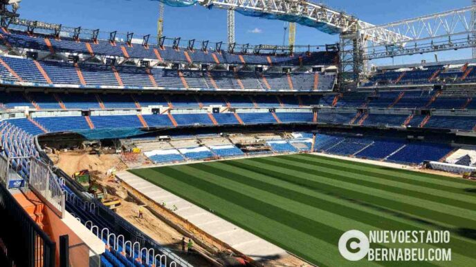 Vista del Estadio Bernabéu en remodelación. Gradas azules, césped con franjas verdes y maquinaria. Vecinos preocupados por las obras y el ruido.