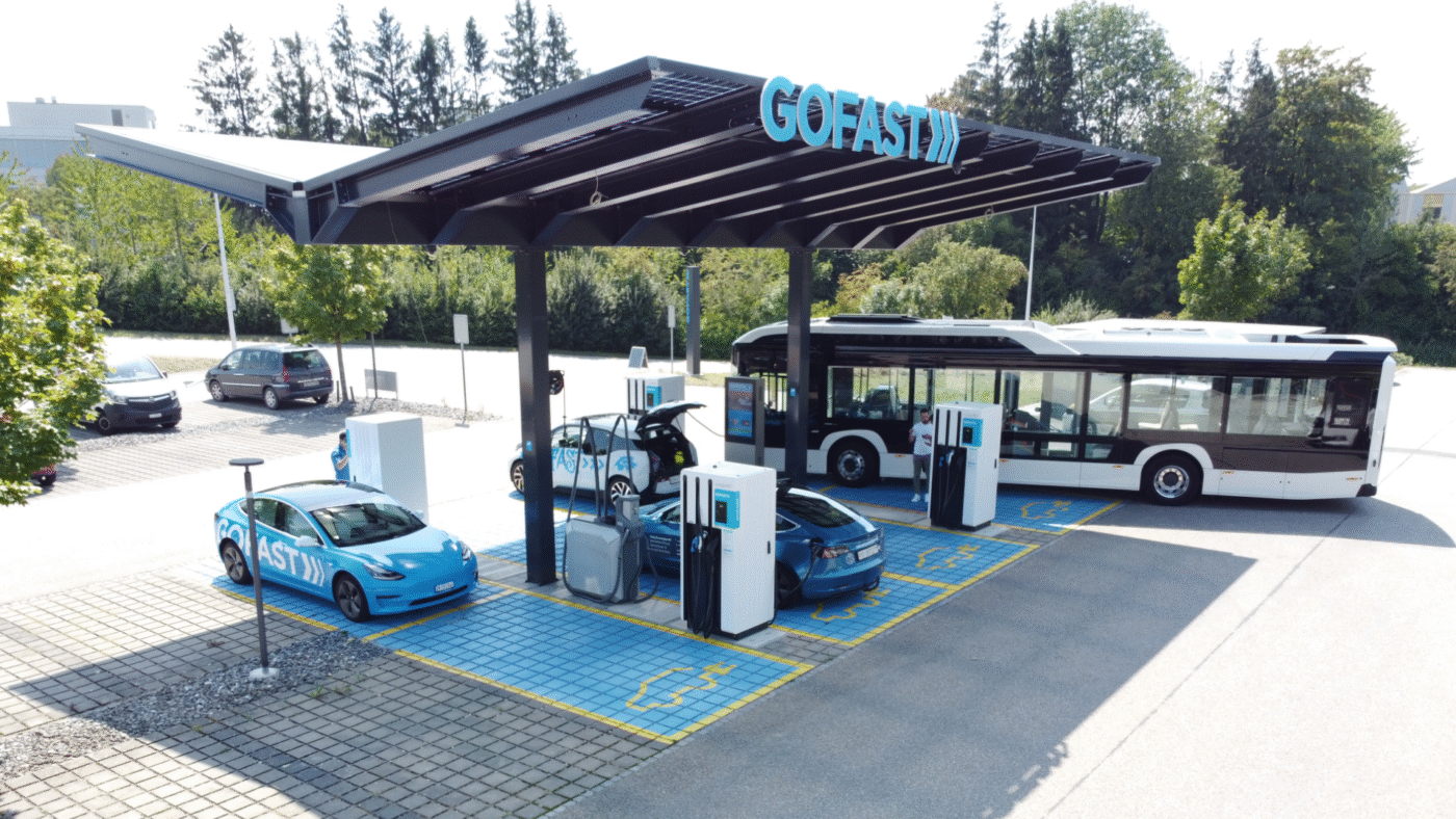 Estación de carga GOFAST con vehículos eléctricos y autobús en Suiza. Infraestructura de carga de alta potencia para coches y transporte público.