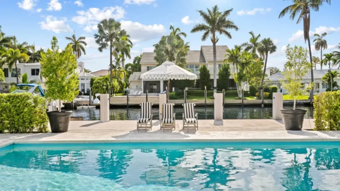 Piscina lujosa con muelle en propiedad de bienes raíces de lujo. Estrategias para maximizar el rendimiento con palmeras y cielo azul reflejado.