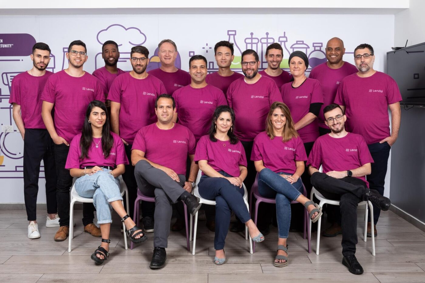 Grupo diverso en Florida, evento inmobiliario Israel. Camisetas moradas 'Lenda', sonriendo, ambiente colaborativo. Inversión y equipo unidos. #Florida