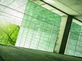 Edificio con fachada de cristal reflejando árboles, ejemplo de construcción sostenible en México. Diseño ecológico e innovador con luz natural.