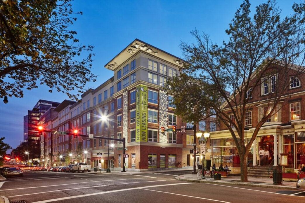 Edificio moderno de vivienda estudiantil HH Group, con letrero de 'Now Leasing', ubicado en una intersección urbana al anochecer. Expansión mercado.