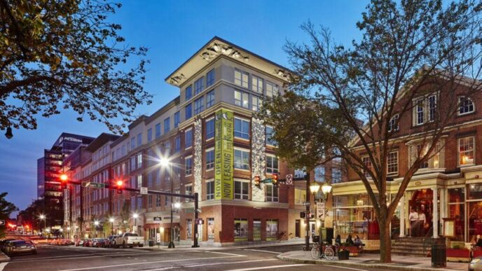 Edificio moderno de vivienda estudiantil HH Group, con letrero de 'Now Leasing', ubicado en una intersección urbana al anochecer. Expansión mercado.