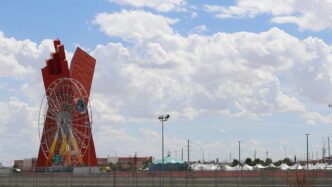 Escultura roja y rueda de la fortuna en Chihuahua, sede de la Feria Nacional de la Construcción con 150 empresas. Cielo azul con nubes.