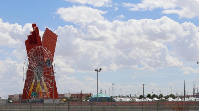 Escultura roja y rueda de la fortuna en Chihuahua, sede de la Feria Nacional de la Construcción con 150 empresas. Cielo azul con nubes.