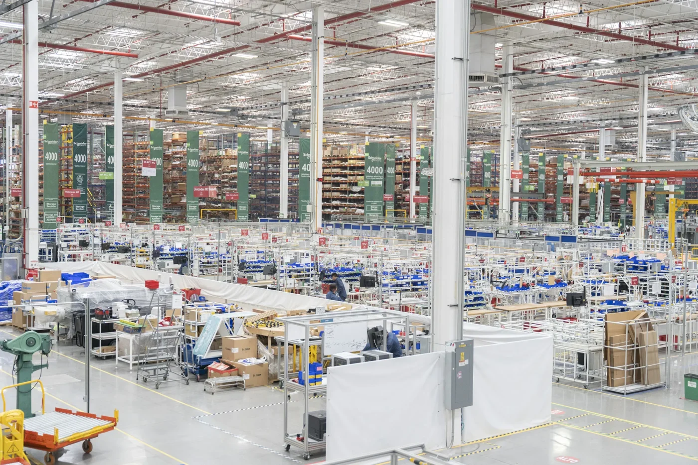 Vista interior de inmueble industrial de Fibra MTY, con estanterías altas y áreas de trabajo. Se visualiza la venta de un espacio de oficinas.