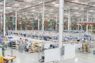 Vista interior de inmueble industrial de Fibra MTY, con estanterías altas y áreas de trabajo. Se visualiza la venta de un espacio de oficinas.