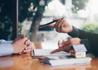 Agente inmobiliario de Clau, la proptech de Flat, explica contrato con pluma y modelo de casa. Inversión y renovación de propiedades.