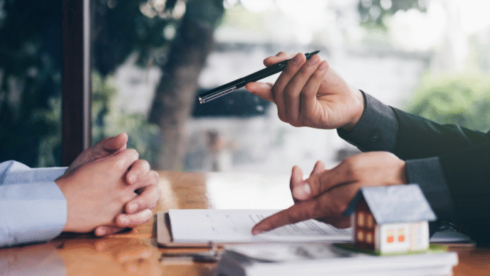 Agente inmobiliario de Clau, la proptech de Flat, explica contrato con pluma y modelo de casa. Inversión y renovación de propiedades.