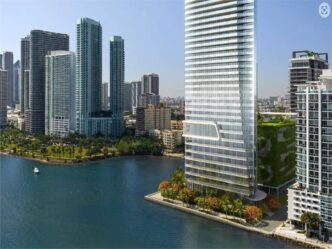 Vista del Edition Residences Miami Edgewater en Florida, torre moderna frente al mar con exuberante vegetación. Arquitectura innovadora y lujo en Edgewater.