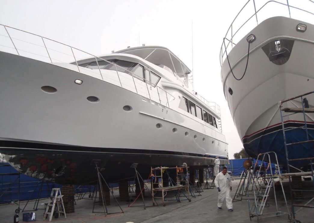 The image doesn't fit any of the specified categories. I will provide a description of the image instead.

Dos yates blancos en dique seco sobre soportes, con un hombre vestido de blanco caminando cerca.