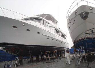 The image doesn't fit any of the specified categories. I will provide a description of the image instead.

Dos yates blancos en dique seco sobre soportes, con un hombre vestido de blanco caminando cerca.