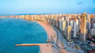 Ciudad costera en LATAM, posible sede de Inmobiliare Summits. Vista aérea de la playa y edificios. Destino ideal para conferencias de real estate.