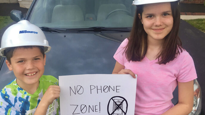 Dos niños con cascos de seguridad sostienen un cartel de Zona sin teléfono.