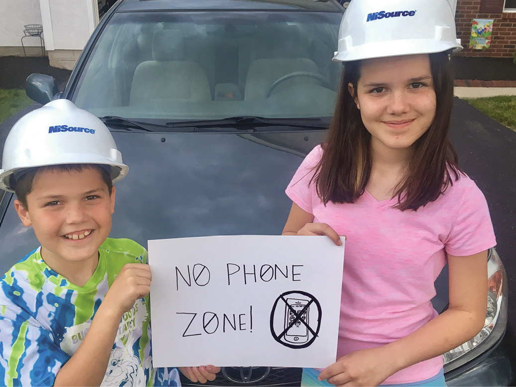 Dos niños con cascos de seguridad sostienen un cartel de Zona sin teléfono.