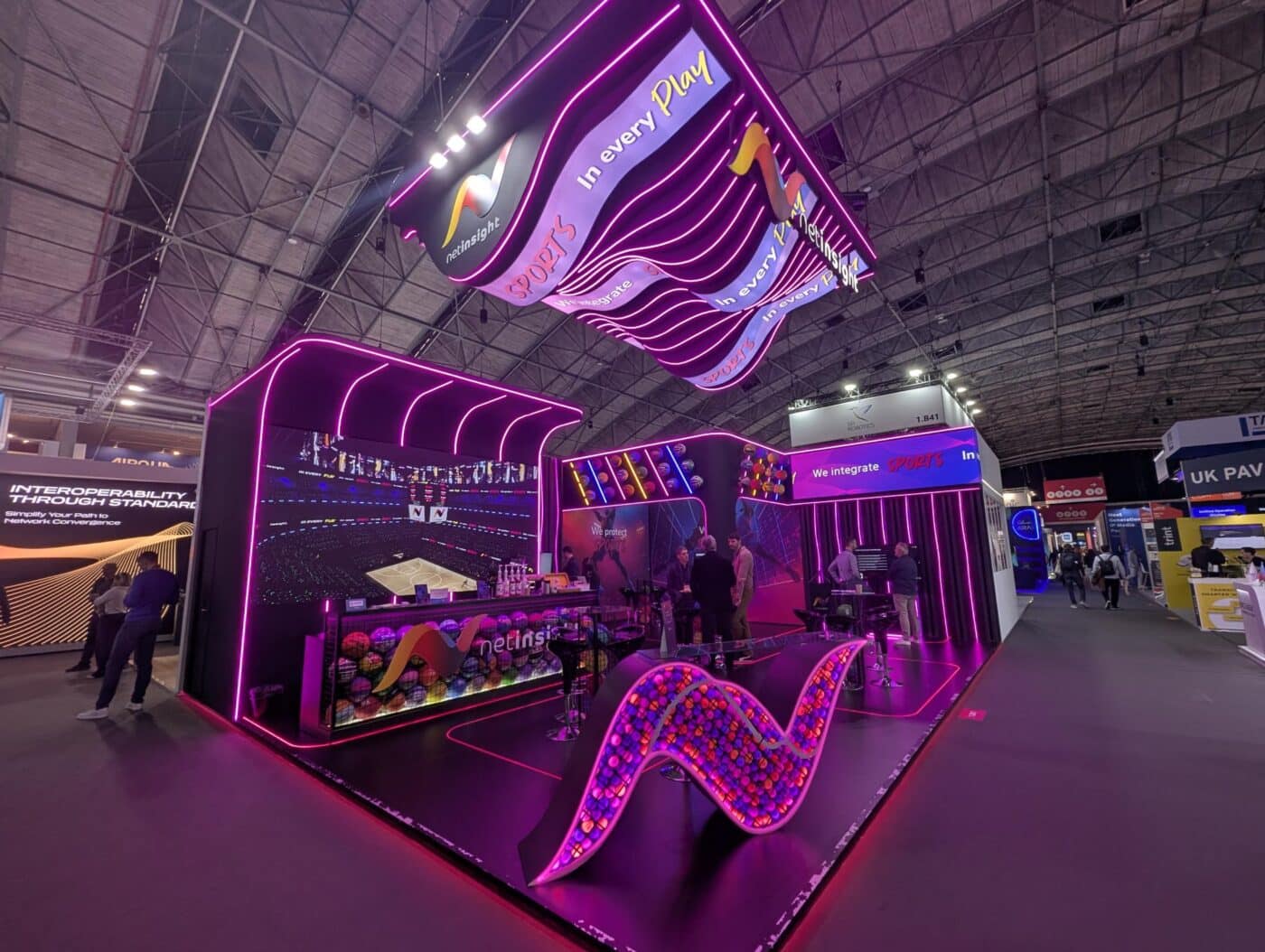 Stand en feria industrial con iluminación neón y logo Netinsight Sports. Diseño moderno e innovador para promoción de inmuebles industriales.