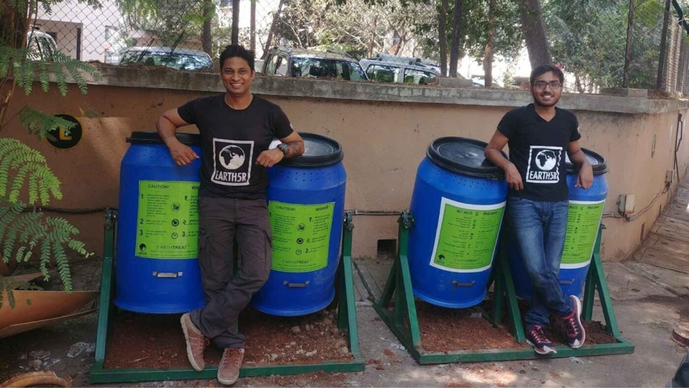 Dos personas junto a contenedores azules para gestión de residuos orgánicos. Solución sostenible para Real Estate con EarthSR. Compostaje eficiente.