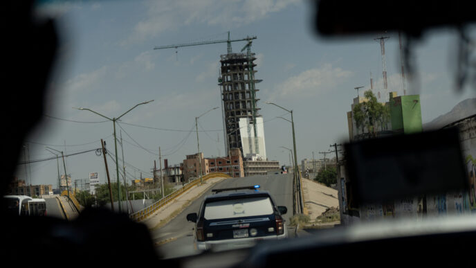 Vista desde vehículo en Ciudad Juárez, Chihuahua: edificio en construcción con grúa, patrulla y paisaje urbano. Gobierno de Chihuahua presente.