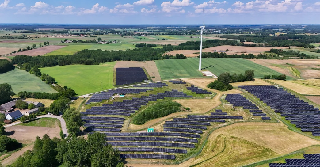 Vista aérea de central híbrida Greenvolt: paneles solares y aerogenerador en campo. Impulso a eficiencia energética y sostenibilidad ambiental.