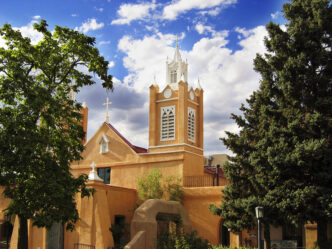 Iglesia histórica con torre blanca y detalles arquitectónicos únicos, bajo un cielo azul con nubes. Arquitectura religiosa prominente.