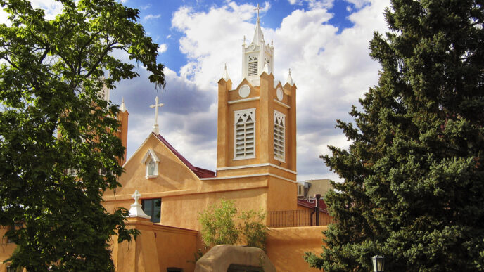 Iglesia histórica con torre blanca y detalles arquitectónicos únicos, bajo un cielo azul con nubes. Arquitectura religiosa prominente.