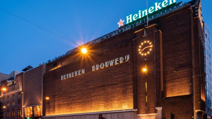 Fachada de la cervecería Heineken en Ámsterdam. Arquitectura de ladrillo con reloj iluminado y letrero de Heineken. Anuncia planta en Yucatán.