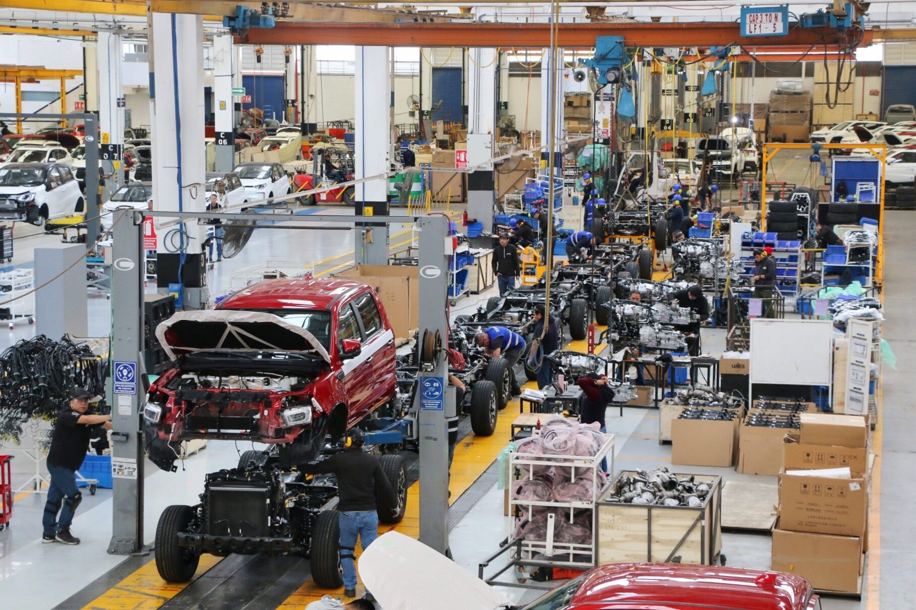 OK. Here's the alt text for the image:

Venue/Architecture

Interior de una fábrica automotriz en México. Línea de ensamblaje con operarios trabajando en varios vehículos.