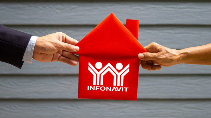 Sponsors/branding.

Manos sostienen figura de casa roja con logo Infonavit. Crédito hipotecario accesible en Inmobiliare Summits, evento de real estate en México.