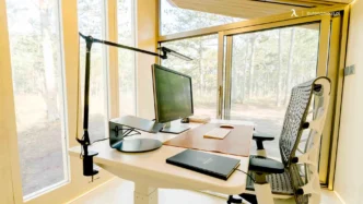 Oficina en casa con escritorio ajustable, monitor y silla ergonómica. Espacio de trabajo moderno y luminoso. Trabajo presencial vs home office.